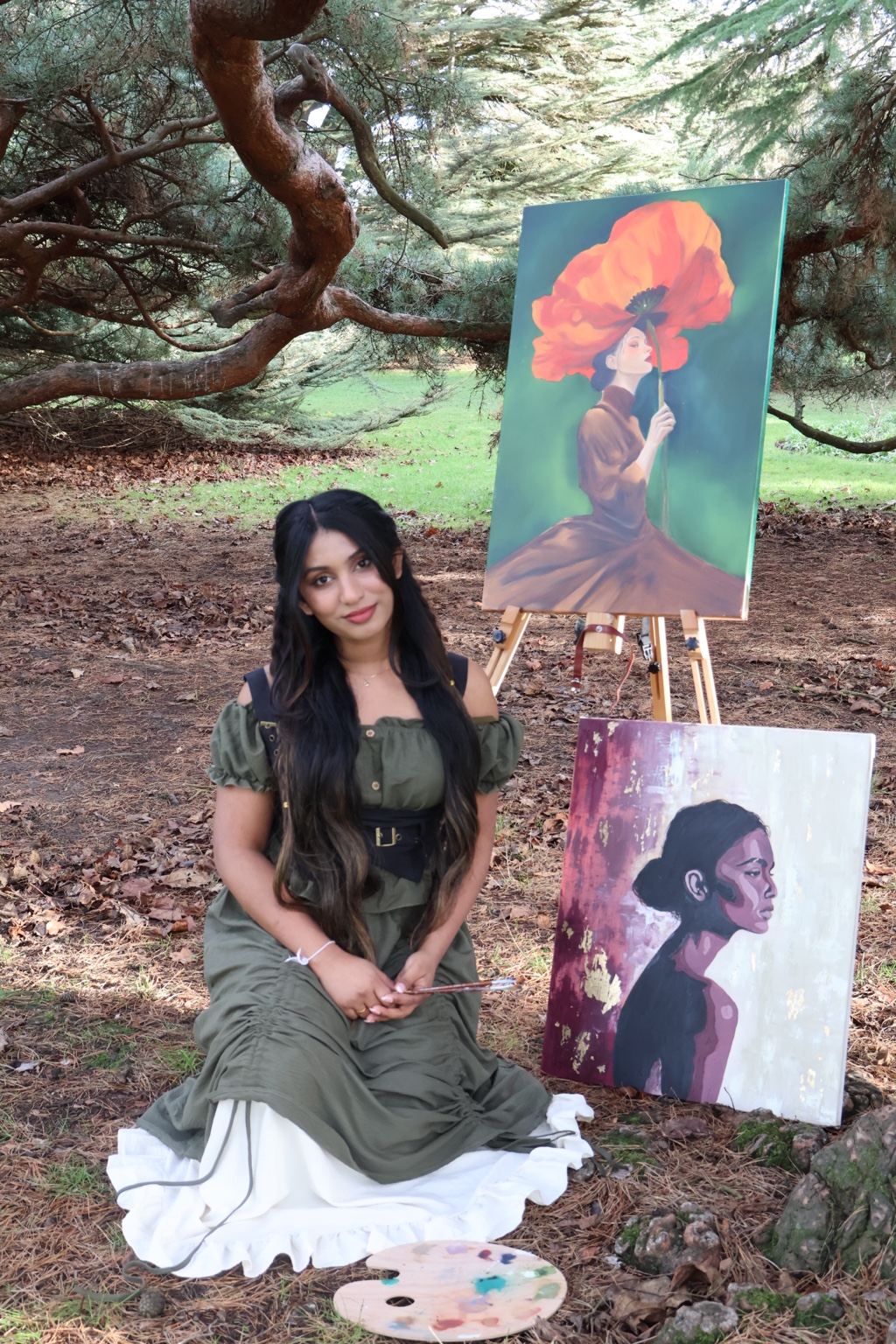 Shehara seated outdoors with two of her oil paintings