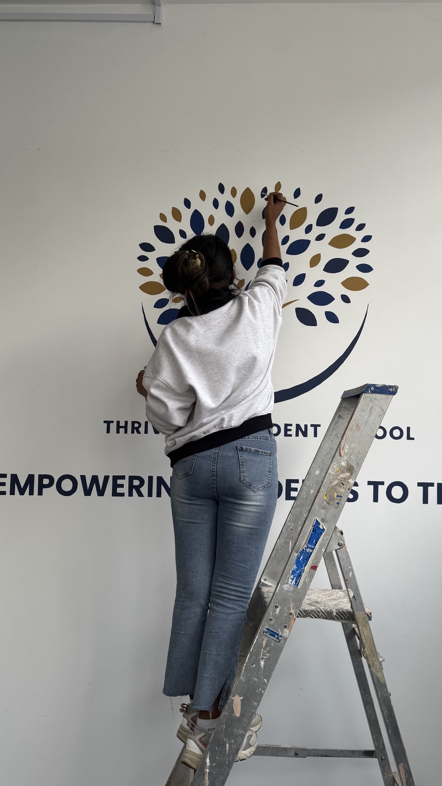 Shehara painting the Thrive Independent School tree mural
